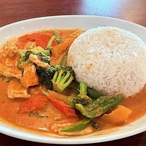 Chicken curry with broccoli, bell peppers, and carrots, served with a side of white rice.