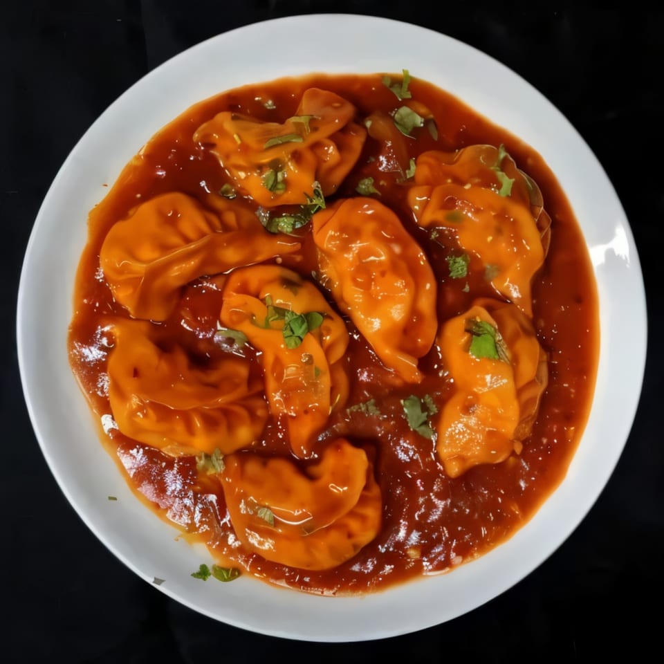 A white plate filled with orange momos in a rich red sauce, garnished with fresh cilantro.