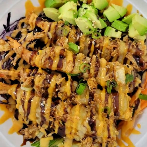 Crispy shrimp tempura drizzled with orange and dark sauces, topped with avocado, sesame seeds, and green onions.