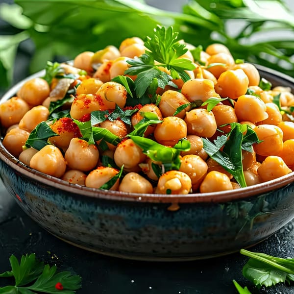 Close-up of a bowl filled with seasoned chickpeas and fresh green herbs.
