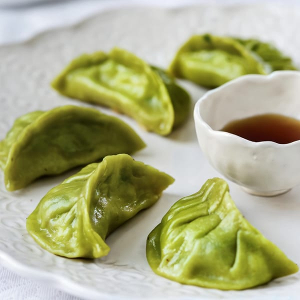 Green dumplings arranged on a white plate with a small bowl of dipping sauce.
