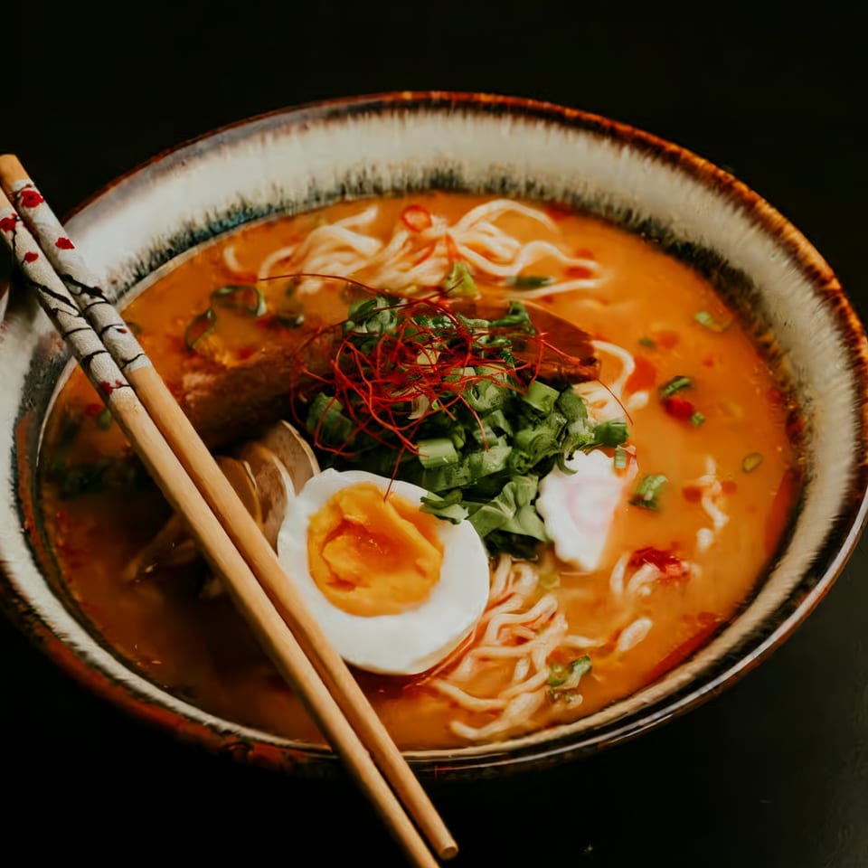 A bowl of ramen with noodles, broth, a soft-boiled egg, green onions, and chili threads.